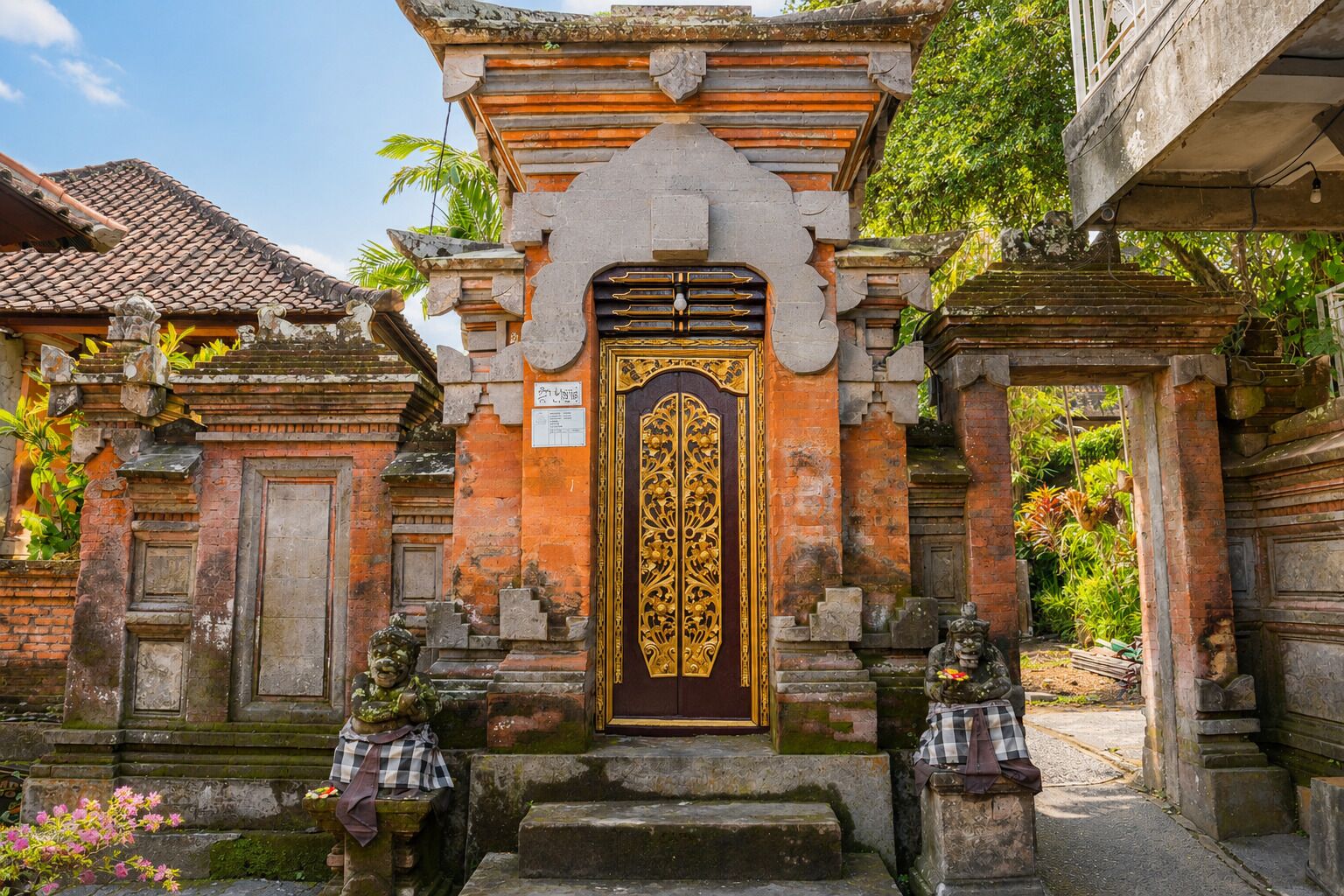 Entrada tradicional de un templo, con una puerta central ricamente decorada, flanqueada por estatuas de piedra y escalones que conducen hacia ella.