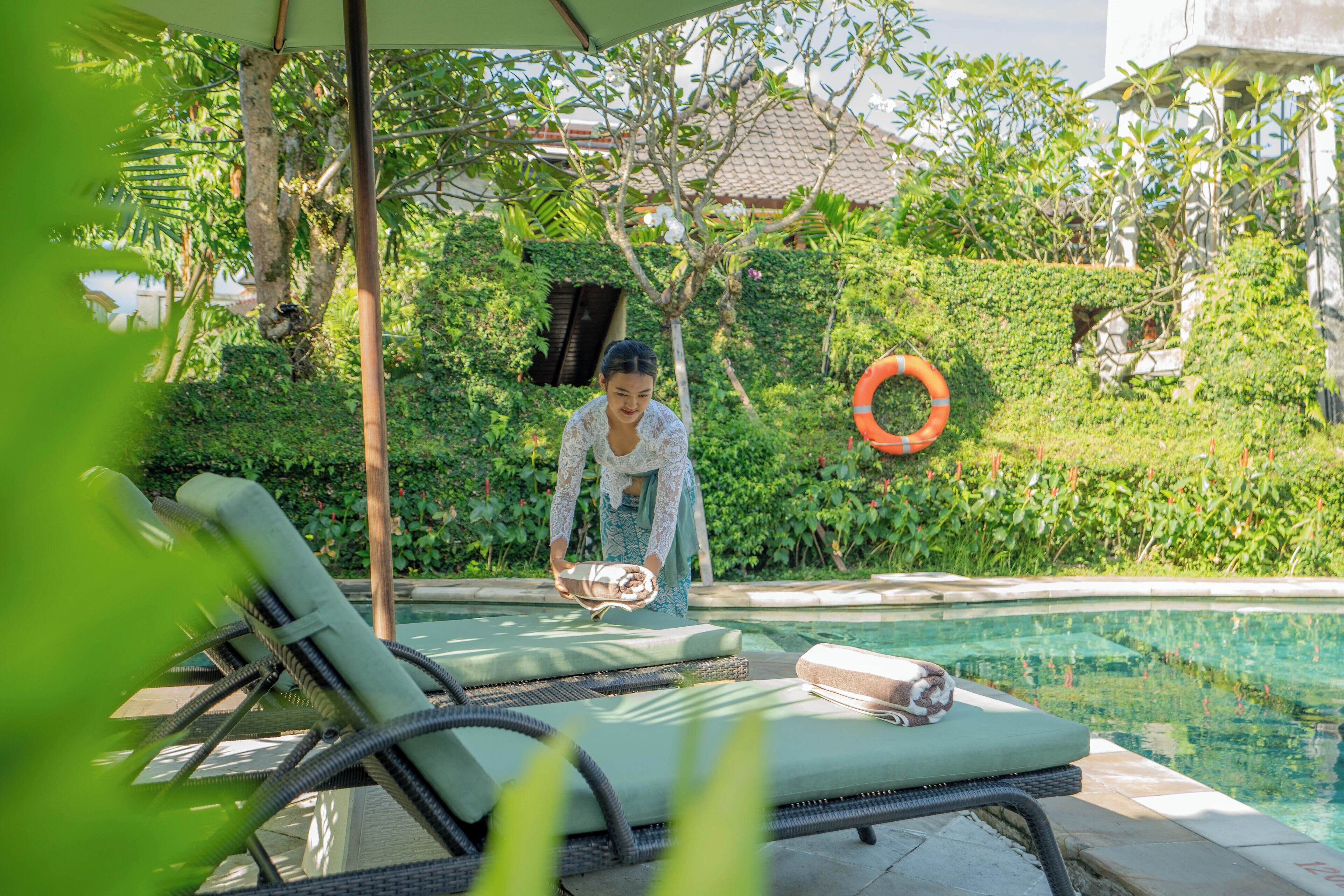 A poolside area with lounge chairs, a pool, and a person tending to the pool.