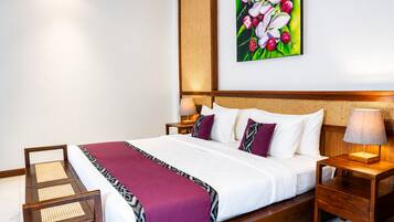 Habitación de hotel con una cama grande, cabecera de madera, mesita de noche con lámpara, una silla y un cuadro colgado en la pared.