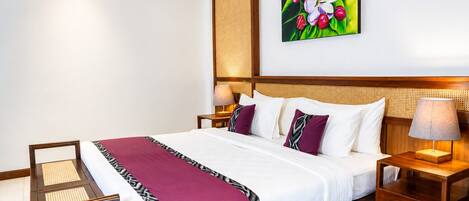 A hotel room with a large bed, a wooden headboard, a nightstand with a lamp, a chair, and a wall-mounted painting.