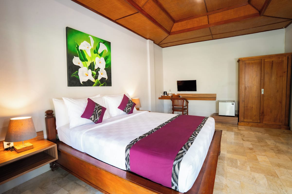 Ein Hotelzimmer mit einem großen Bett, einem Flachbildfernseher, einem Holzschrank und einem Blumenbild an der Wand.