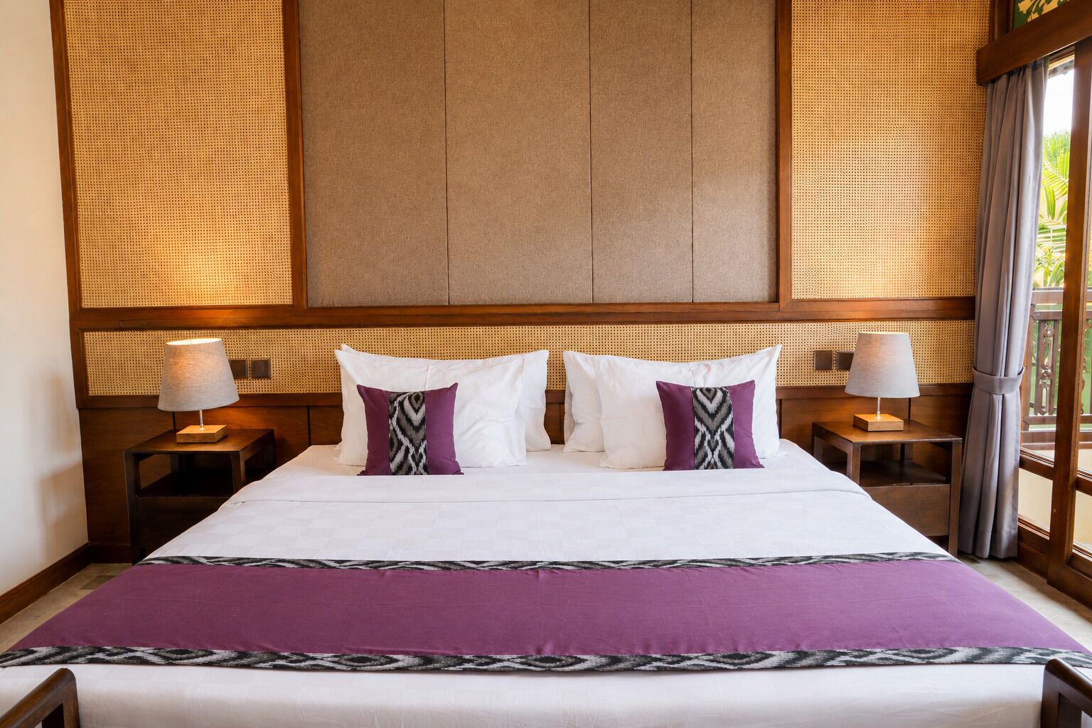 Een hotelkamer met een groot bed, twee nachtkastjes en een raam met gordijnen.