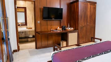 A hotel room with a bed, a TV mounted on the wall, a wooden wardrobe, and a small desk with a chair.