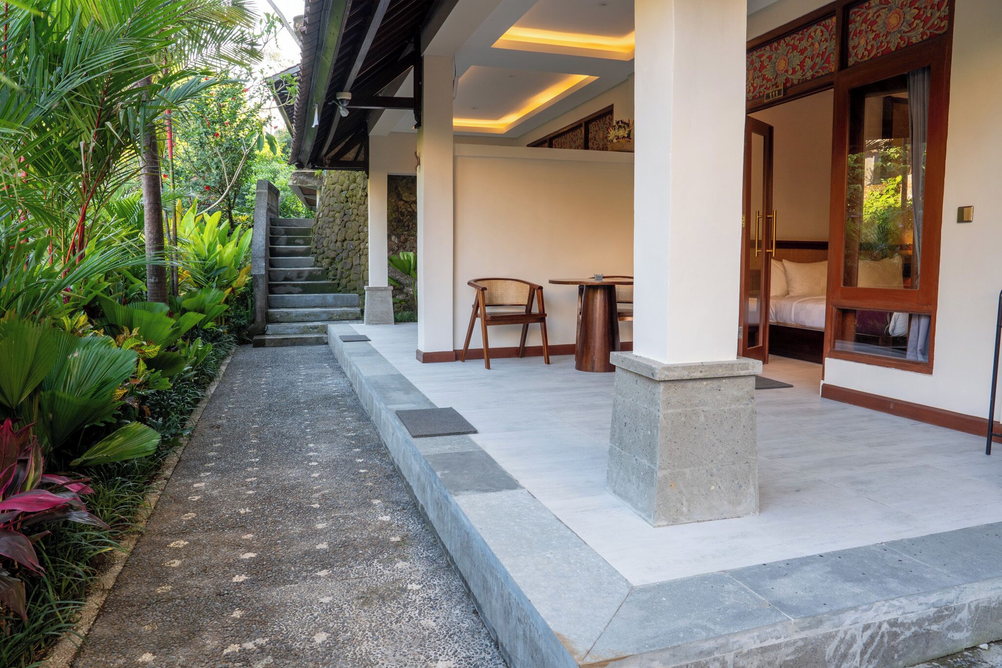 A covered outdoor area with a stone staircase, a wooden bench, and a bed visible through a glass door.