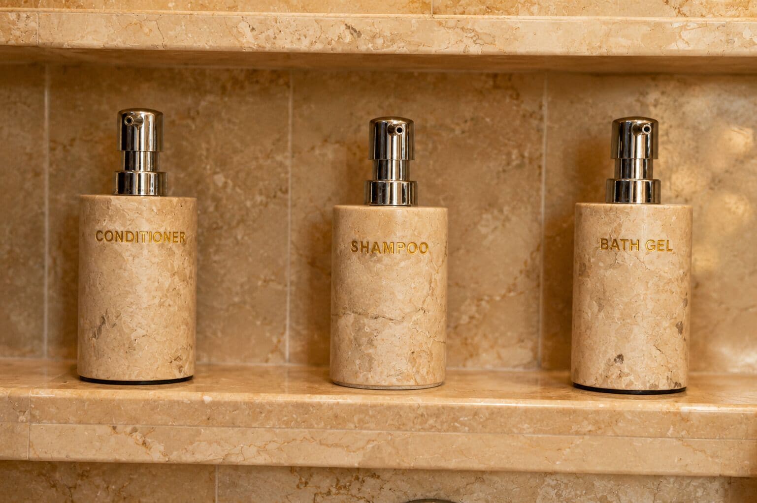 Three toiletry bottles on a marble shelf.