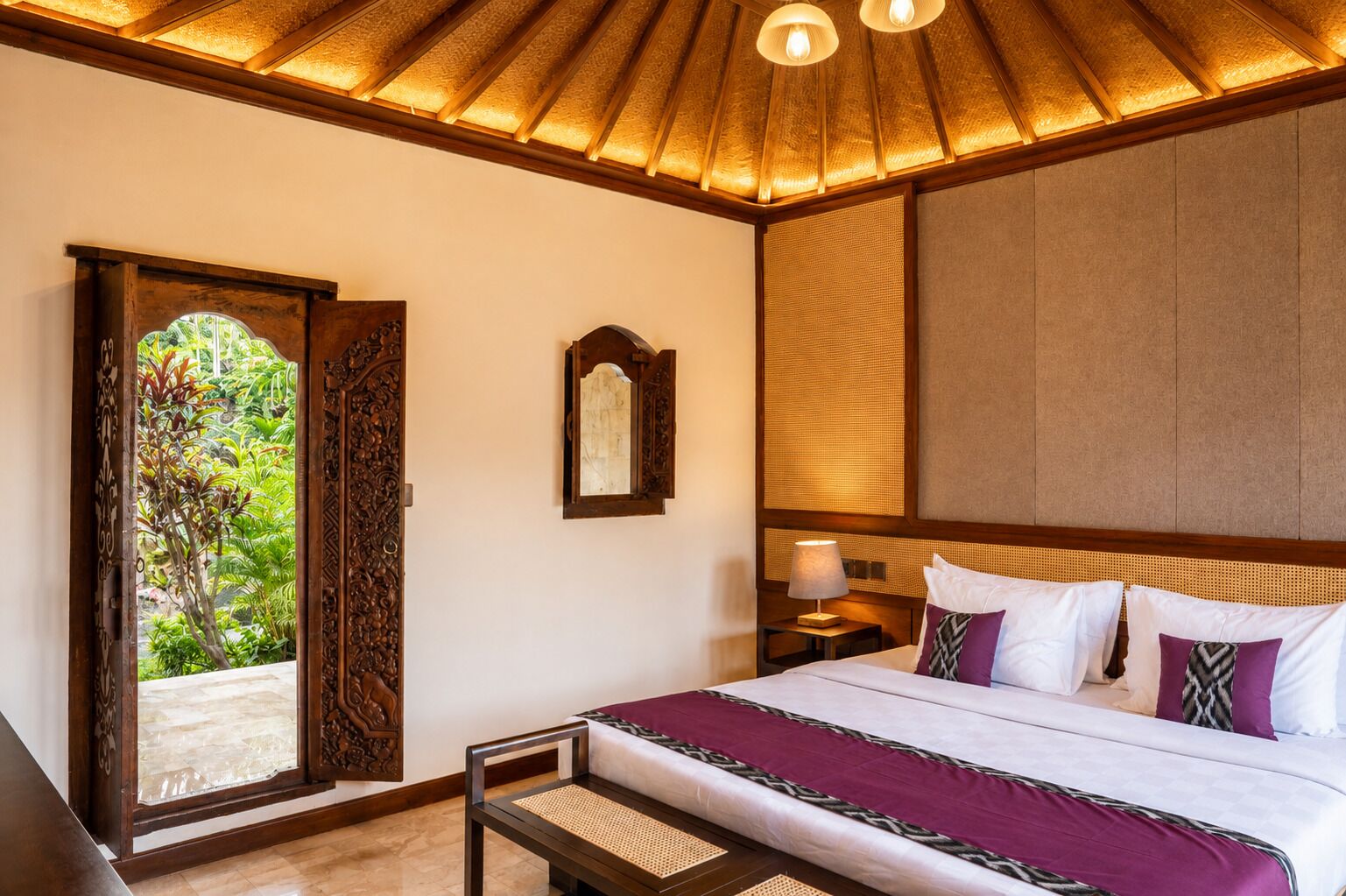 A hotel room with a bed, a nightstand, a lamp, a wooden chair, and a large window with a view of greenery.