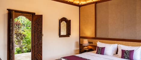 A hotel room with a bed, a nightstand, a lamp, a wooden chair, and a large window with a view of greenery.