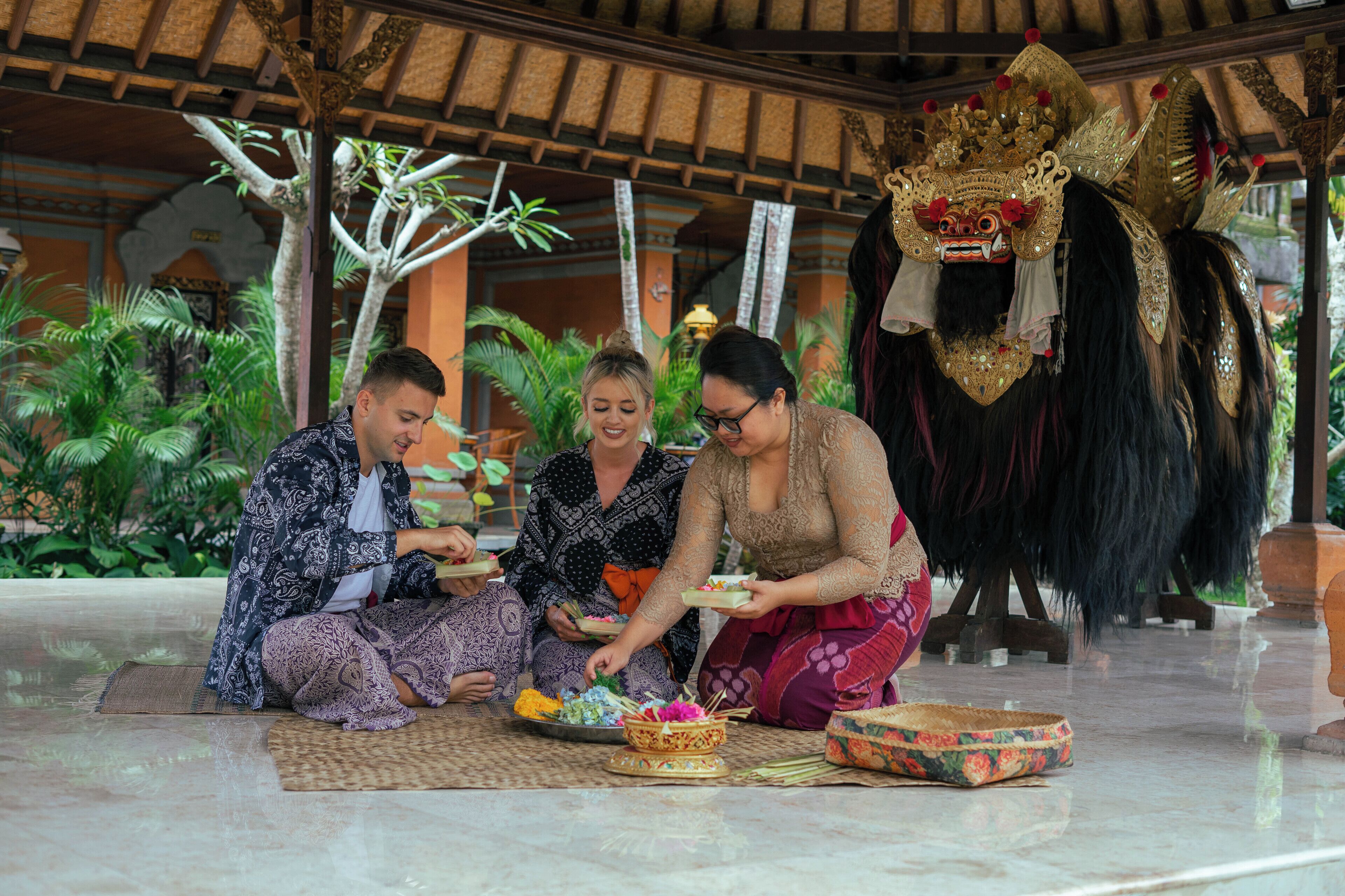 Un groupe de personnes est assis par terre et participe à une cérémonie culturelle, portant des vêtements traditionnels et un masque cérémoniel.