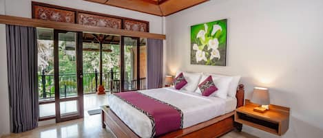 A spacious bedroom with a large bed, a nightstand with a lamp, and a view of greenery through the sliding glass doors.