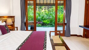 A hotel room with a bed, a nightstand, a desk, and a view of lush greenery. - Mumbul Ubud (Ubud)