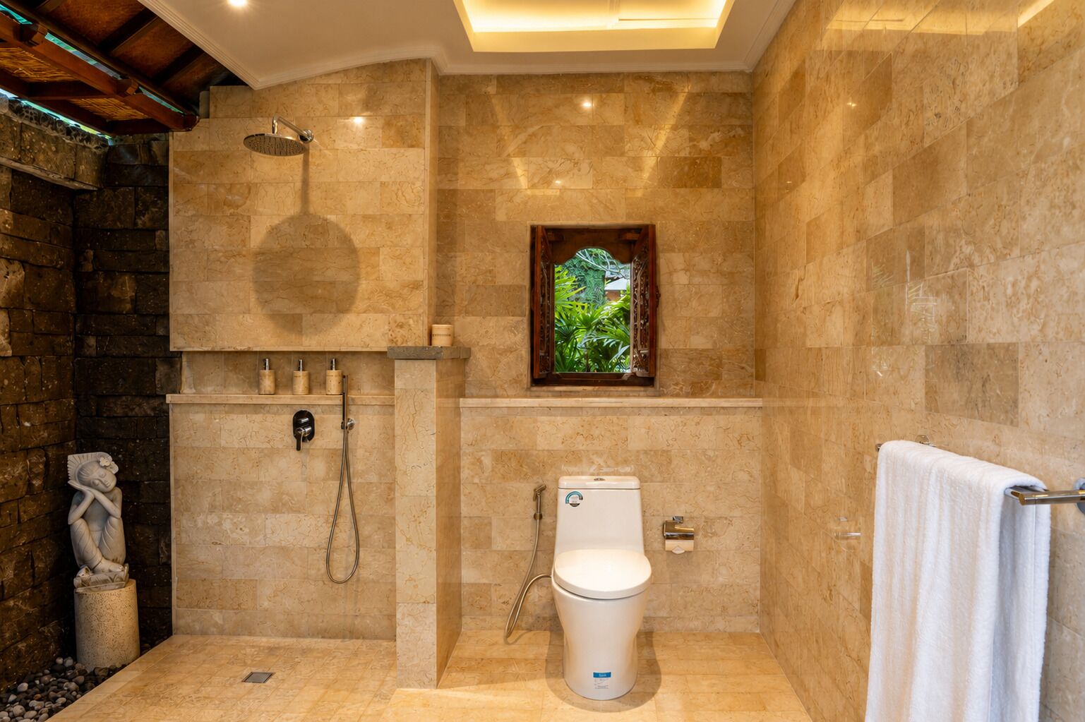 A bathroom with a stone wall, a shower, a toilet, and a window with a view of greenery.