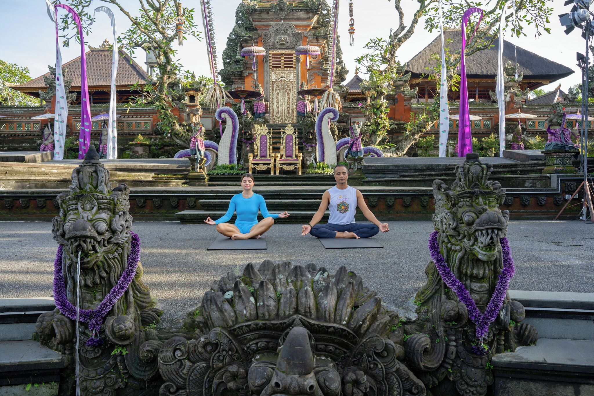 Two individuals meditating on mats in front of ornate stone carvings.