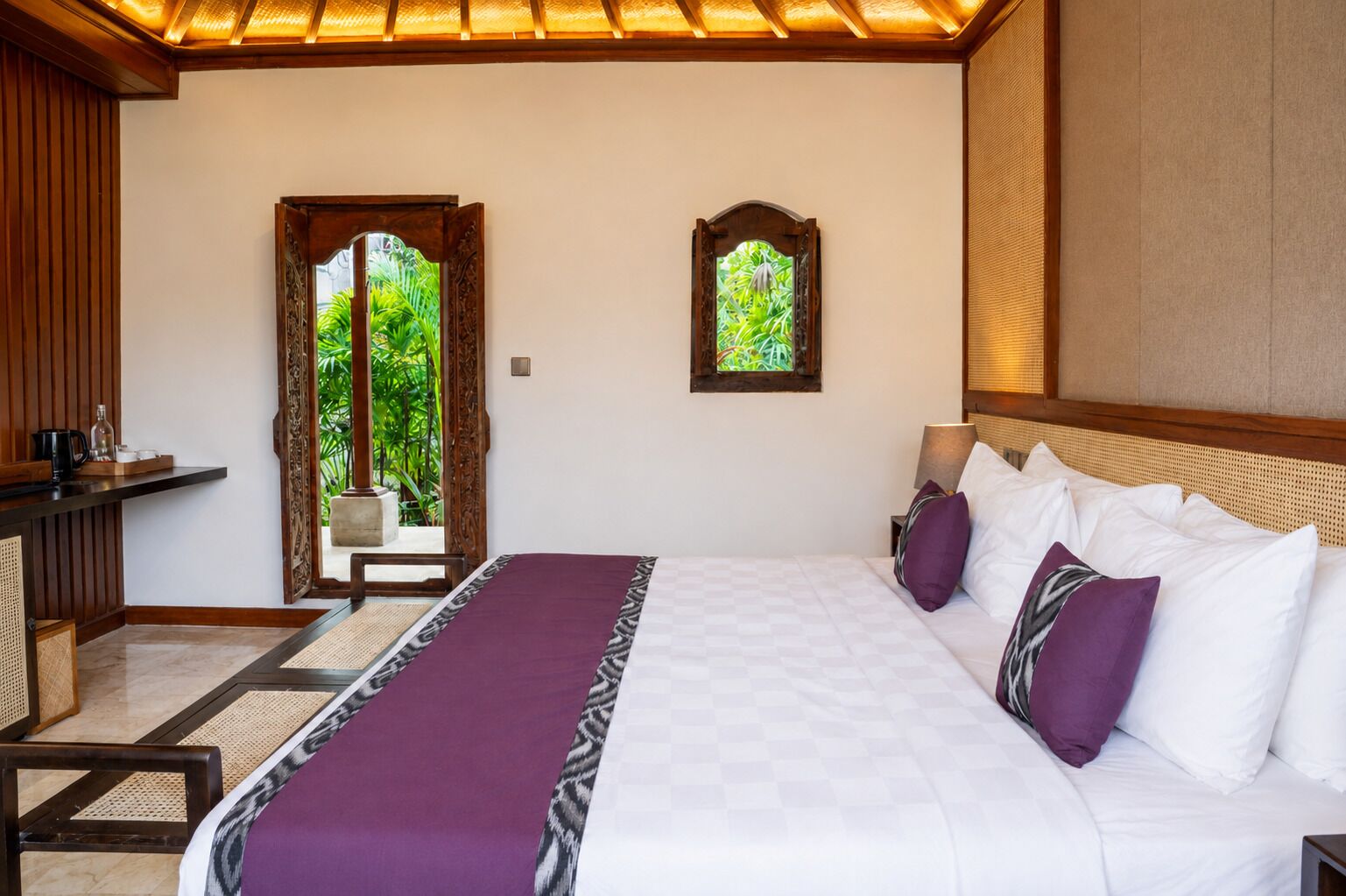 A bedroom with a bed, bedside table, and a view of greenery through a window.