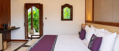 A bedroom with a bed, bedside table, and a view of greenery through a window.