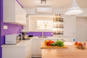 A modern kitchen with white cabinets, a purple wall, a window with a view, and a wooden countertop with vegetables.