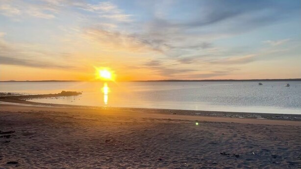 Une plage au coucher du soleil, avec un ciel dégagé et une eau calme.