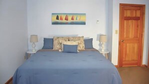 Une chambre à coucher avec un lit, deux tables de chevet, une porte en bois et un tableau au mur.
