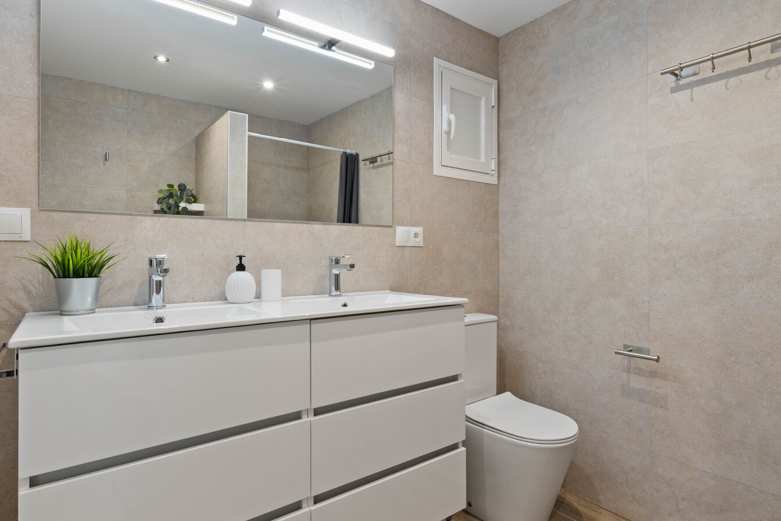 A modern bathroom with a double sink vanity, a toilet, and a large mirror.
