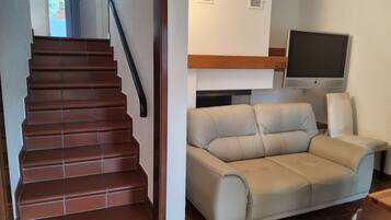 A staircase with brown steps and a black handrail, a beige sofa, a television on the wall, and a window with blinds.