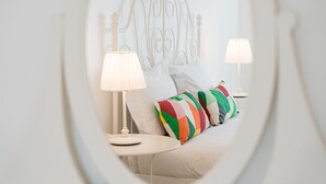 Un dormitorio con cabecera de metal blanco, dos mesitas de noche con lámparas y coloridas almohadas a rayas.