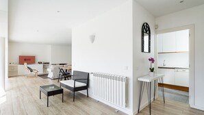 Una sala de estar moderna con un sofá, dos sillones, una mesa de centro y una zona de cocina con un lavamanos y encimera.