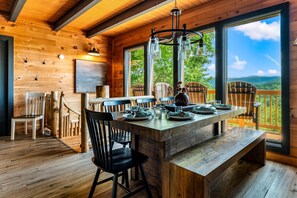 Interno di una baita in legno con un tavolo da pranzo, sedie e un'ampia finestra che si affaccia sull'esterno.