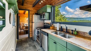 A modern kitchen with green cabinets, stainless steel appliances, and a large window offering a scenic view.