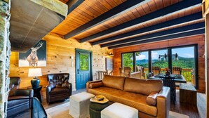 A log cabin interior with a leather sofa, leather chairs, a dining table, and a view of the outdoors.