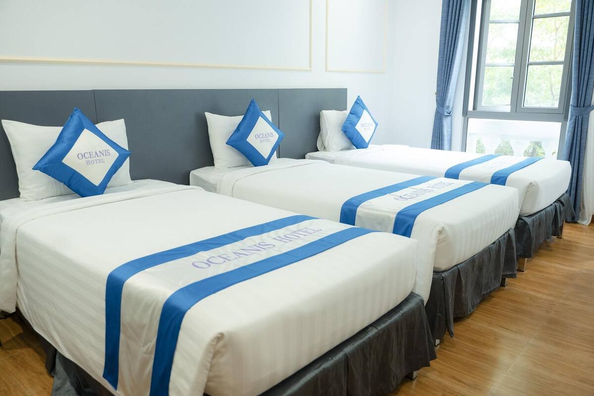 A hotel room with three beds, each with a blue and white bedspread and matching pillows.