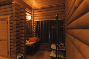 Ein Holzblockhaus-Innenraum mit einer Holzbänkl, einem Waschbecken mit orangenem Becken und einem hängenden Gestell.