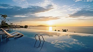 Una piscina infinita con vistas a la puesta de sol sobre el océano, sillas de descanso y palmeras.