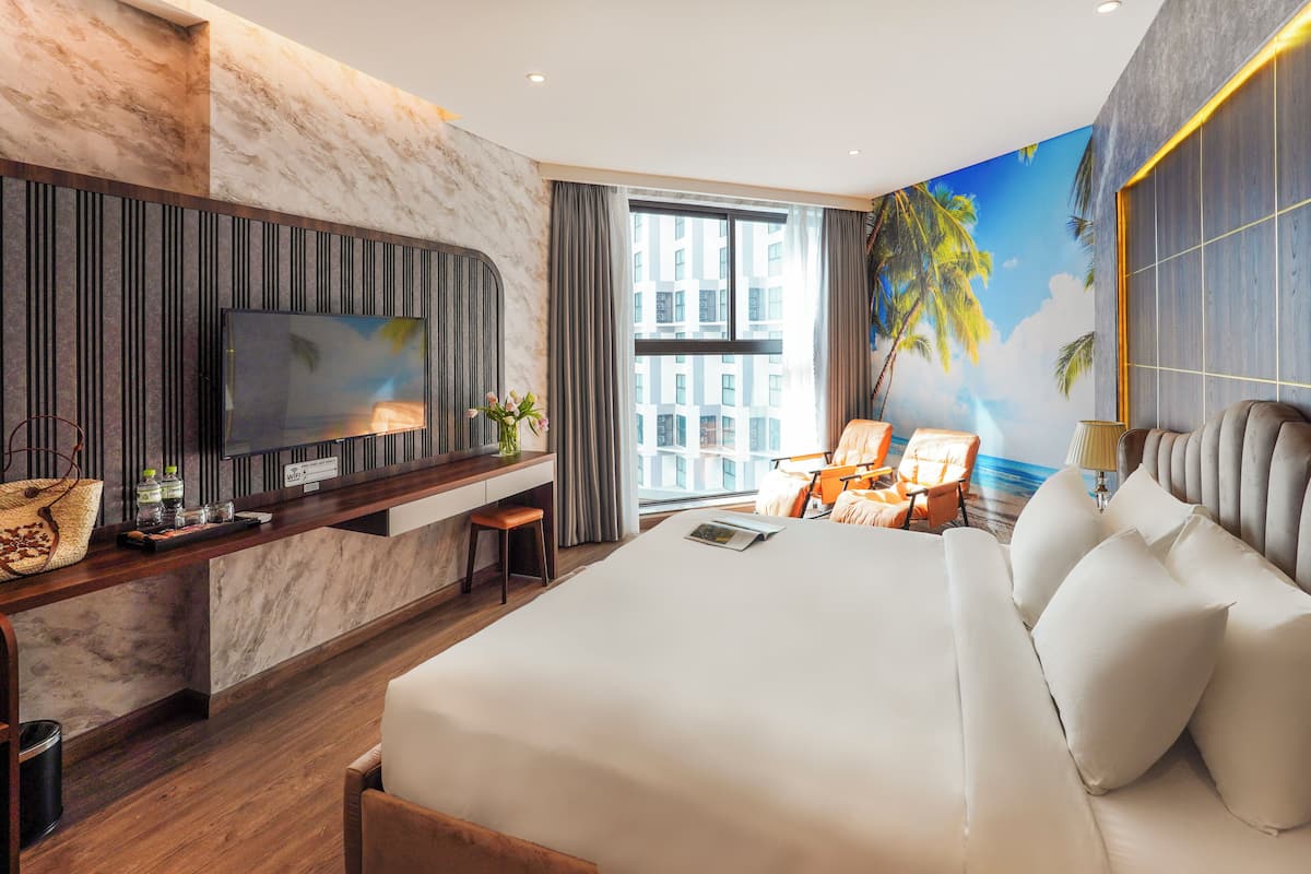 A modern hotel room with a large bed, a TV, a desk with a computer, and a mural of a beach scene.