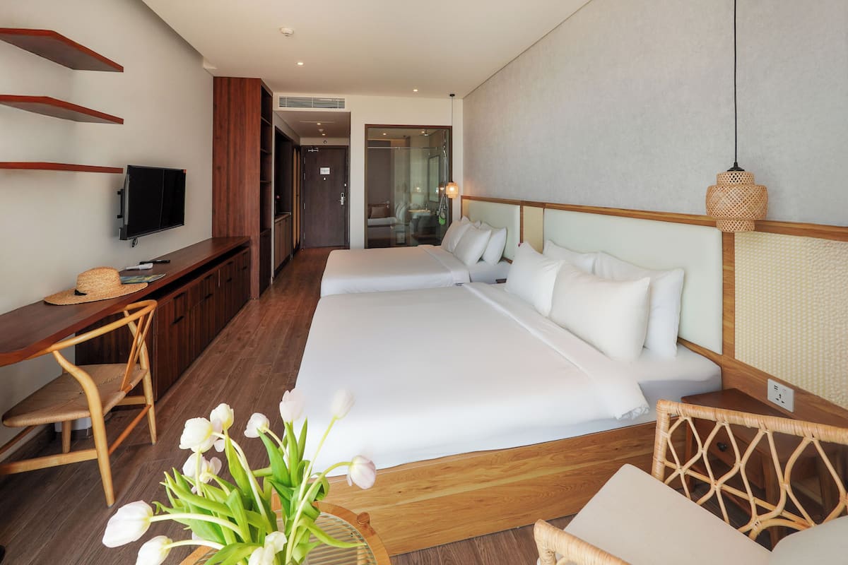 A hotel room with a large bed, a desk with a chair, a television, and a vase of flowers.