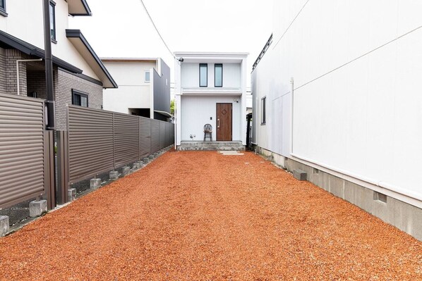 Une ruelle étroite, avec un chemin de gravier menant à un bâtiment doté d’une porte en bois et d’un petit porche.