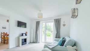Una sala de estar moderna con un sofá, un televisor de pantalla plana, una chimenea y un ventanal con cortinas.