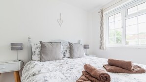 Una cama bien hecha con ropa de cama floral, dos lámparas de noche y un ventanal con cortinas.