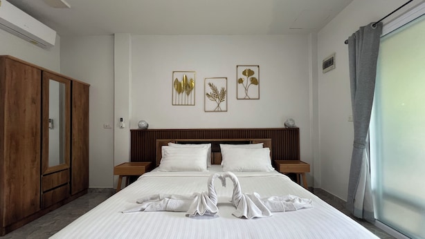 A hotel room with a large bed, wooden headboard, two bedside tables, a wardrobe, and two framed botanical prints on the wall. - Cozy near Samui airport (Chang Wat Surat Thani)