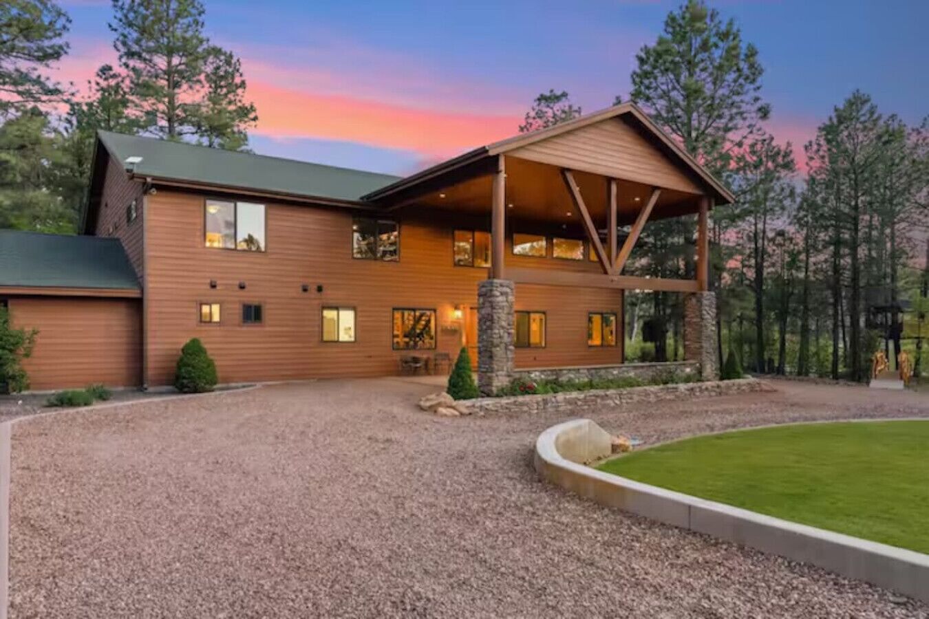 A two-story log cabin with a covered porch, a stone fireplace, and a well-maintained gravel driveway.