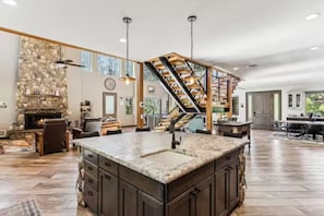 A spacious living area with a large island, a stone fireplace, and a staircase leading to an upper level. - Richardson Rock Creek Ranch (Show Low)