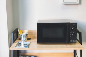 A black microwave on a wooden table with a metal bucket containing a yellow cup and a straw.