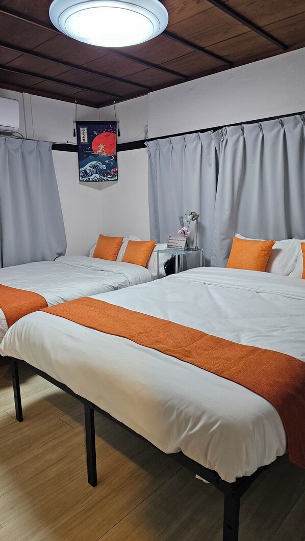 Ein Hotelzimmer mit zwei Betten, grauen Vorhängen, einem Wandbild und einem kleinen Tisch mit einer Lampe.