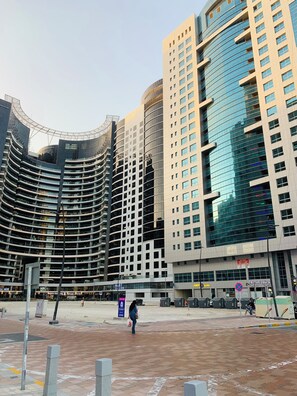 A modern urban plaza with high-rise buildings, a central open space, and a few pedestrians.