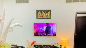 Un comedor con una mesa, sillas, un florero con flores, un televisor y una obra de arte colgada en la pared.
