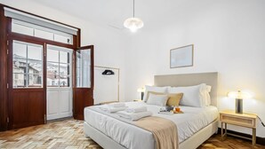 Een hotelkamer met een groot bed, een houten visgraatvloer, een uitzicht door een glazen deur en een nachtkastje met een lamp.