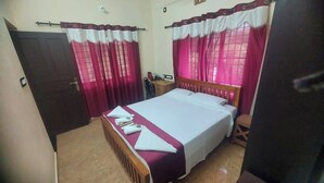 Ein Schlafzimmer mit Bett, Vorhängen, einem hölzernen Kopfteil, einem Nachttisch und einem kleinen Hocker.