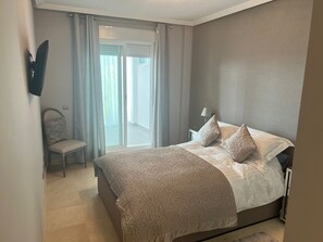 Ein Schlafzimmer mit einem Bett, einem Sessel, einer Lampe und Blick durch ein Fenster.