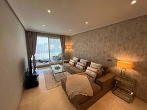 Ein modernes Wohnzimmer mit einer Couch, einem Glastisch, einer Lampe und Blick durch eine Schiebetür auf einen Außenbereich.