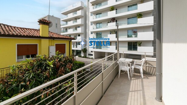 A balcony with white chairs, a yellow building, and a white apartment building with balconies. - Marchioretto Apt. - * Beach place and Parking * (Jesolo)