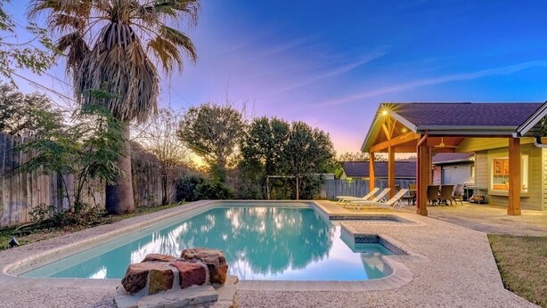A rectangular swimming pool with a hot tub, surrounded by a wooden fence and palm trees. - “Spacious 4BR Home with Private Pool Perfect for Families!” (San Antonio)