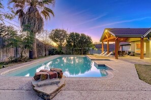 Ein rechteckiger Pool mit Whirlpool, umgeben von einem Holzzaun und Palmen.